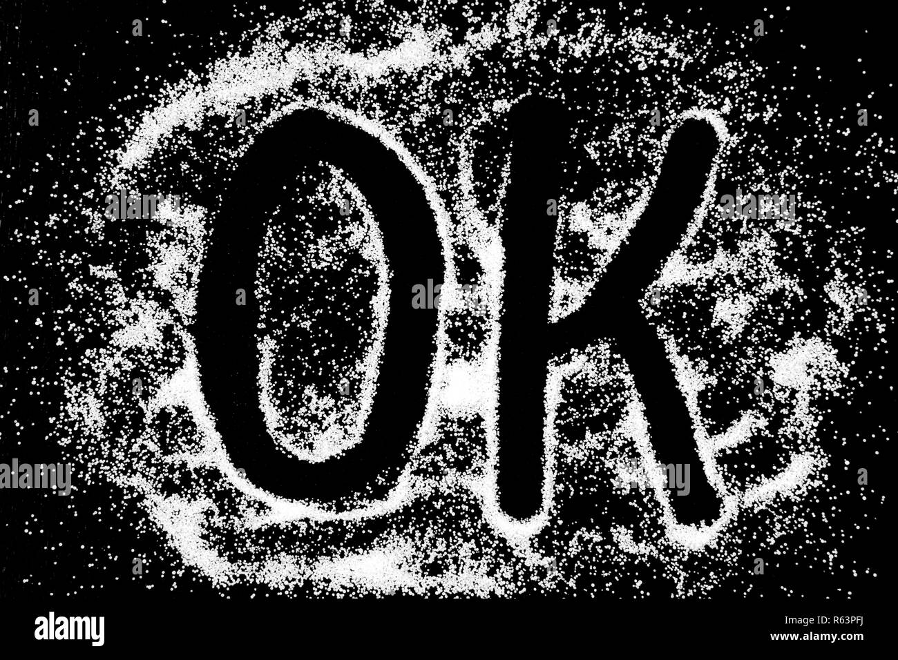 OK palabra símbolo dibujo por dedo en nieve polvo de sal blanca sobre fondo negro. Letras mayúsculas Foto de stock