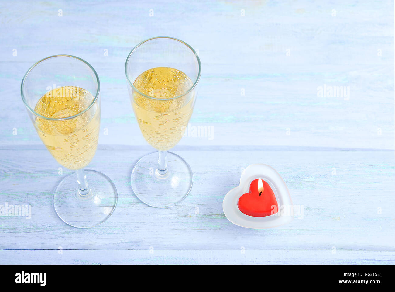 Dos copas de champaña y un corazón rojo con forma de vela. Azul de fondo de madera. Foto de stock