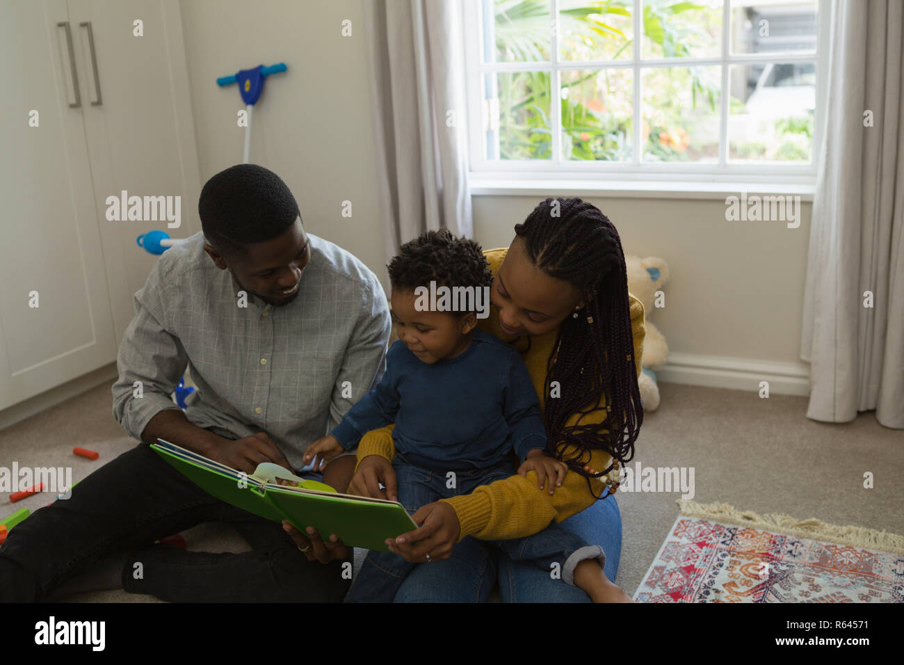 Padres leyendo un libro de imágenes con su hijo en un salón Foto de stock