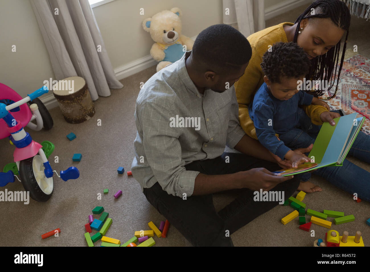 Padres leyendo un libro de imágenes con su hijo en un salón Foto de stock