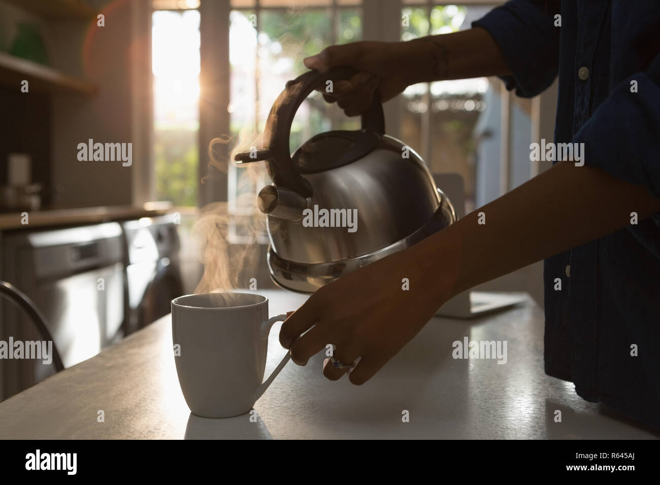 Mujer llenar la taza con agua caliente en la cocina Foto de stock