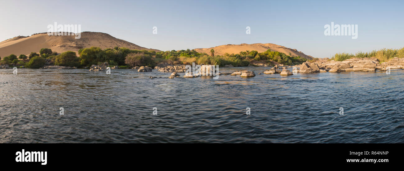 Ver abajo gran anchura del río Nilo en Asuán Egipto a través de la campiña rural paisaje con catarata rocosas islas y fondo de montaña Foto de stock