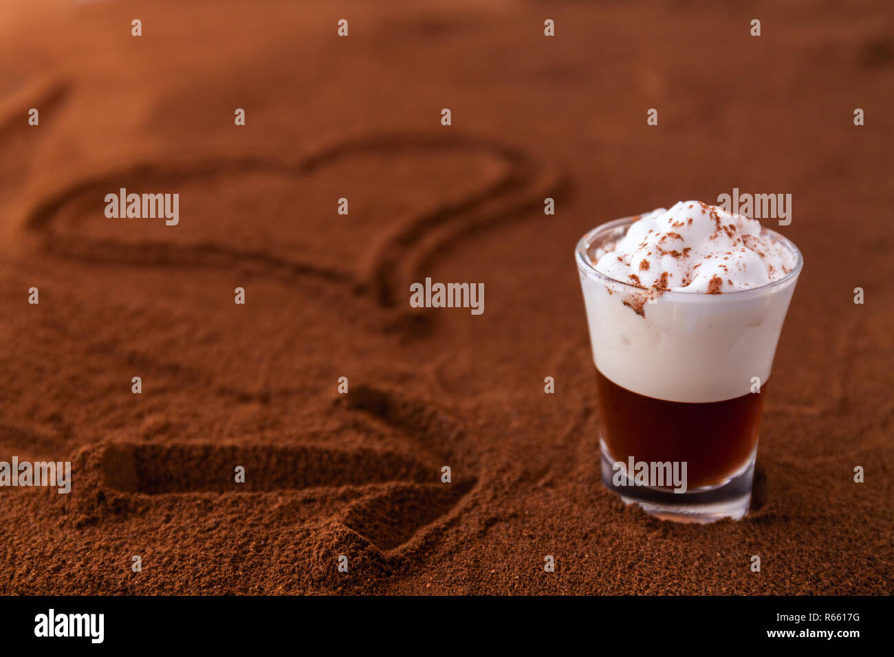 Poco taza de piccolo latte macchiato sobre una mesa cubierta con el corazón y la flecha sobre el café molido como fondo Foto de stock
