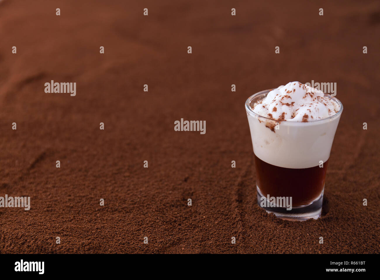 Poco taza de piccolo latte macchiato sobre una mesa cubierta con café molido como fondo Foto de stock