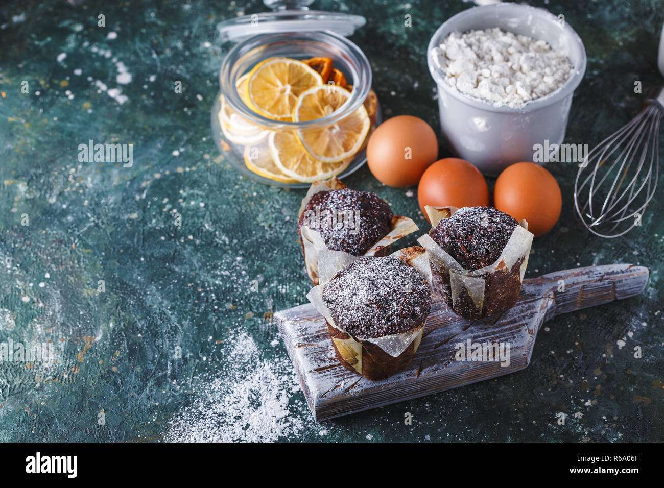 Zanahoria muffin de chocolate espolvoreado con azúcar impalpable, una taza de té, ingredientes para hornear. Harina, huevo, limón citrus sobre una tabla, copia espacio oscuro Foto de stock