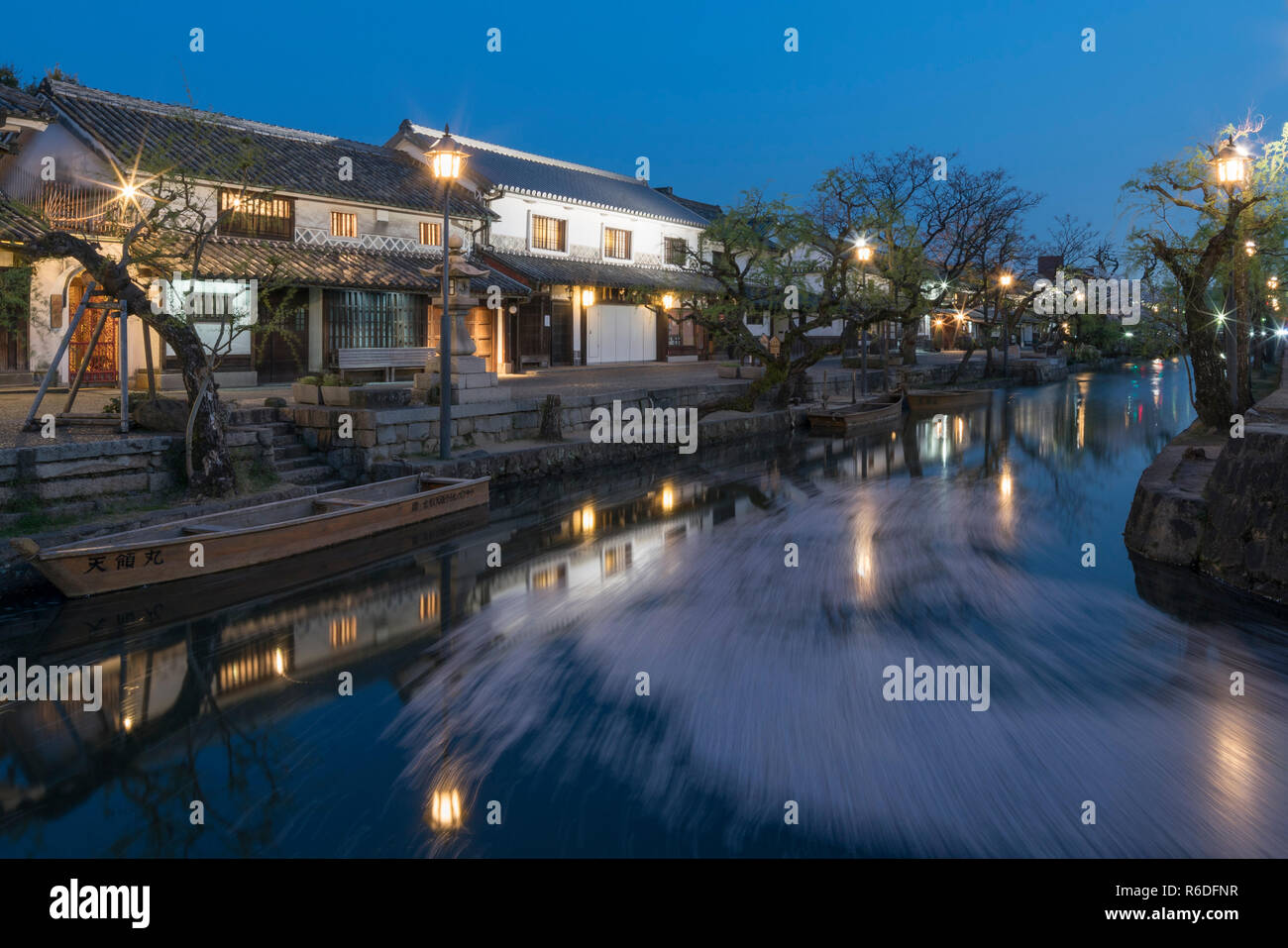 Flujo de pétalos de flores de cerezo en el canal del barrio histórico Bikan por la noche, Kurashiki, Japón Foto de stock