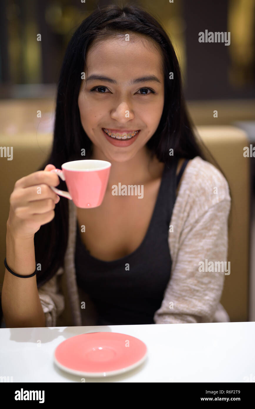 Feliz mujer asiática hermosa joven relajándose en el interior de la tienda de café Foto de stock