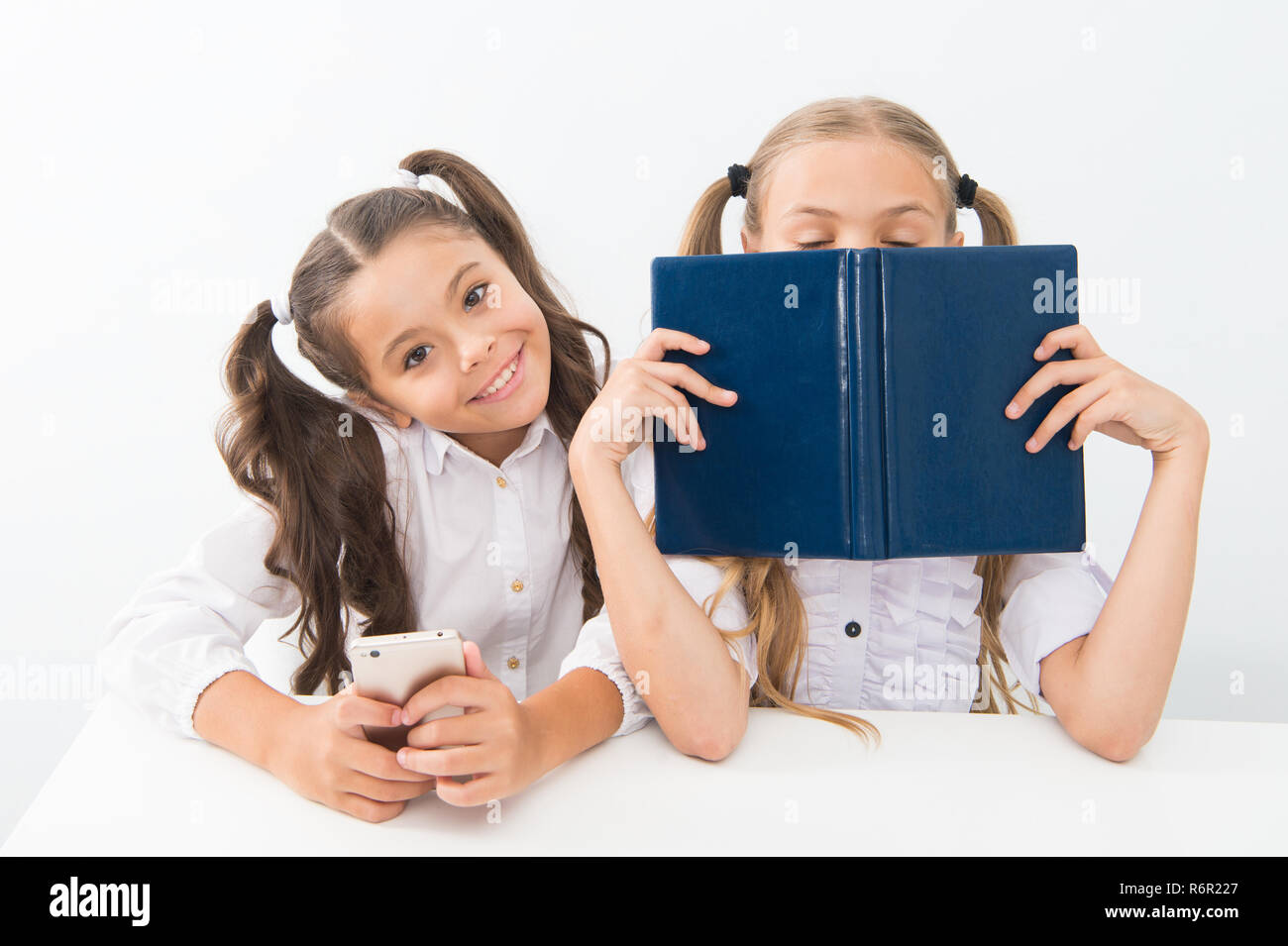 Contra la vieja escuela moderna. Colegiala mantenga teléfono móvil smartphone moderno mientras su amiga disfrute de libro viejo como almacenamiento de datos analógicos. Tecnología contra la experiencia. Nueva generación de demandas educativas. Foto de stock