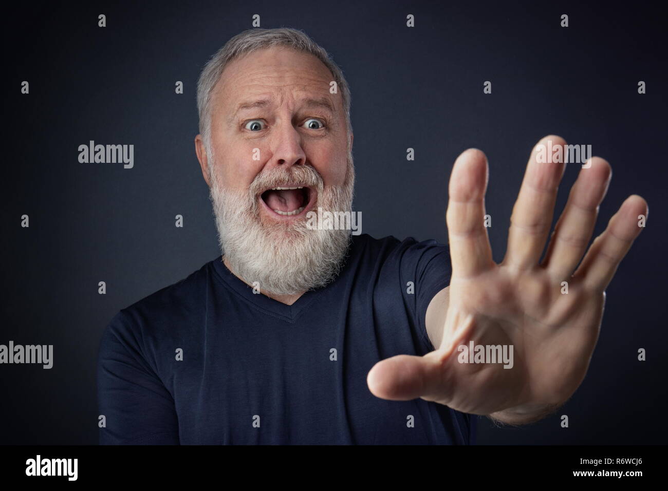 Anciano en camisa y asustada con su mano estirada hacia adelante para parar algo Foto de stock