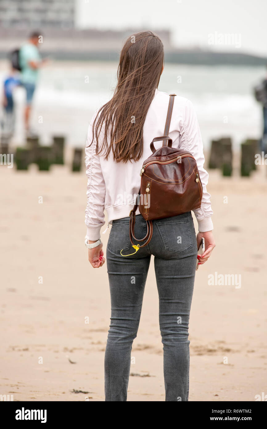 Mujer joven con largo pelo castaño se encuentra en la playa y lleva una  mochila marrón sobre su espalda Fotografía de stock - Alamy