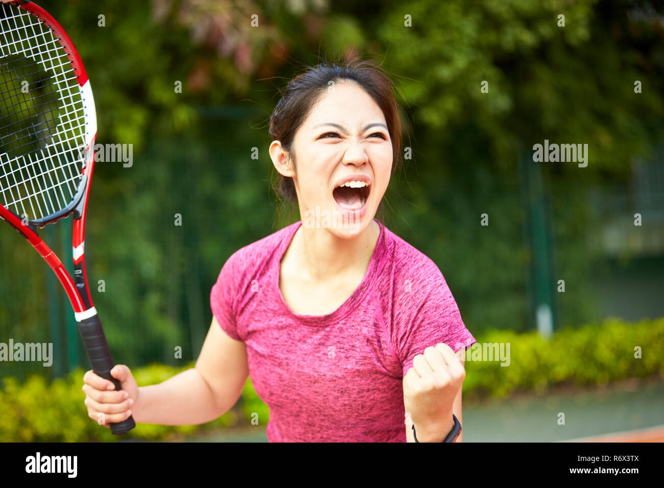 Joven asiática jugador de tenis femenino celebrando después de marcar un punto Foto de stock