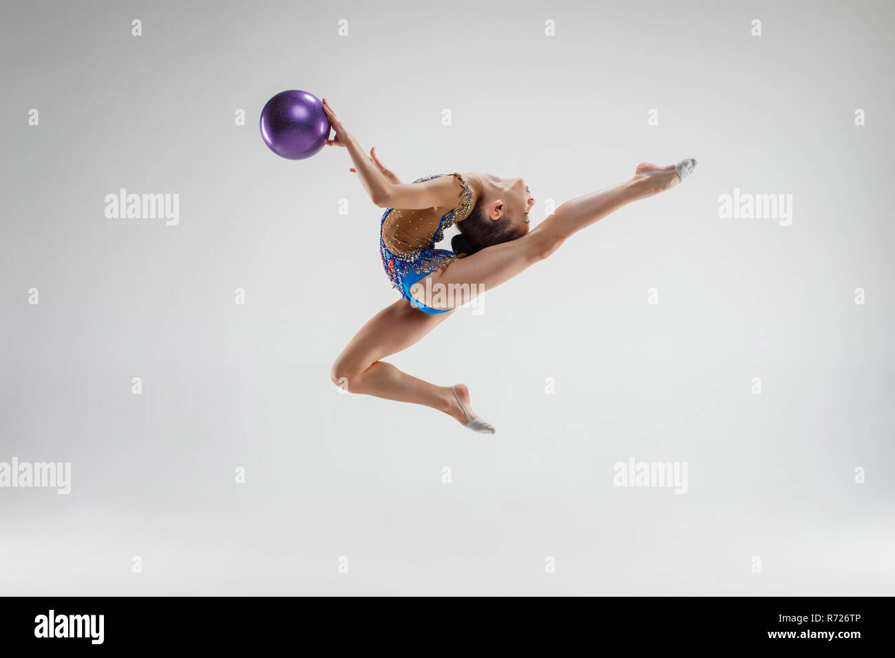 Una niña de gimnasia rítmica en un traje negro realiza ejercicios con una  pelota