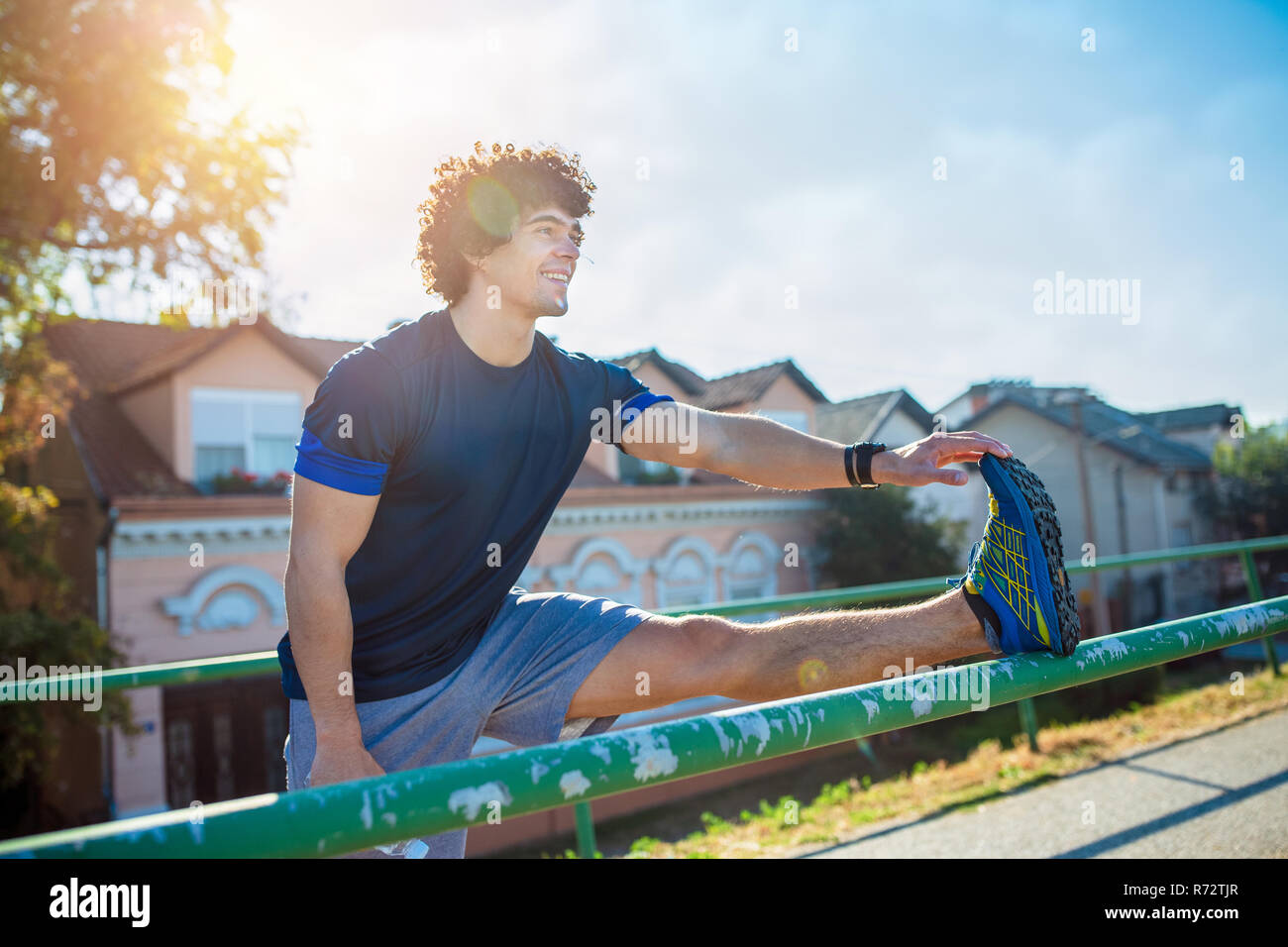 Fitness sonriente hombre haciendo ejercicio de estiramiento, preparación para el entrenamiento en el parque Foto de stock