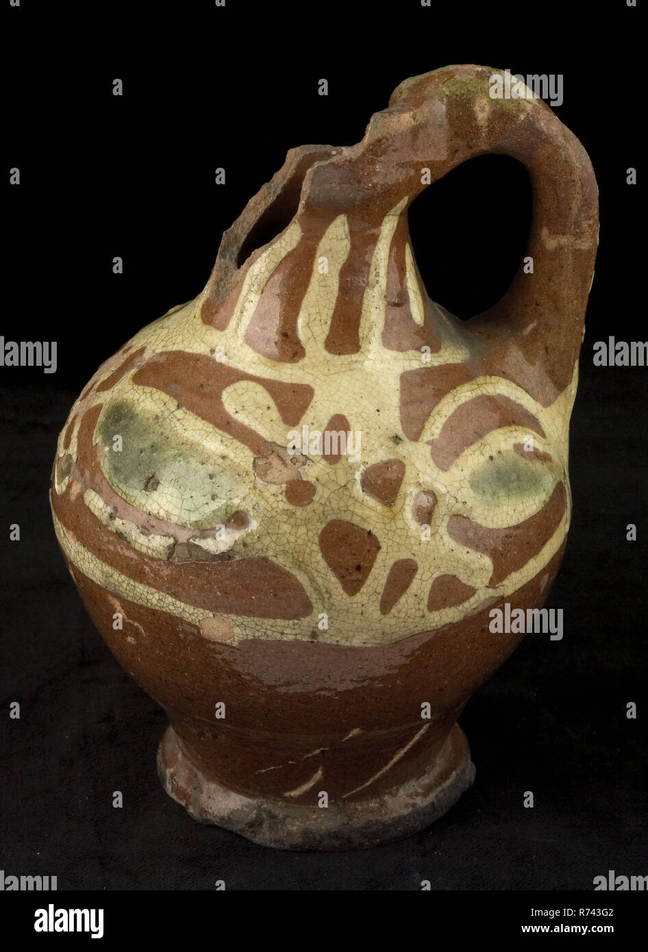 Jarra de aceite de barro con mango y oído permanente, decoración de seda alrededor del cuello, hombros, vientre y oiljug titular de vajilla de cerámica glaseada suelo encontrar loza de barro vidriado de plomo, anillo 6.4 gira a mano decorado limonada frito aceite de cerámica vidriada jarra sobre el pedestal. Con forma de bola cuello delgado borde del cuello con puño collar. Red shard totalmente acristalado decorado en los lodos técnica decoración consiste de amarillo con arcos cruzados en el Oriente verdes campos con forma de ojo en el hombro rayas amarillas en la nuca y sobre las orejas. Girar los labios sobre el vientre. Roetsporen. Crooked archeol oído permanente adjunta Foto de stock