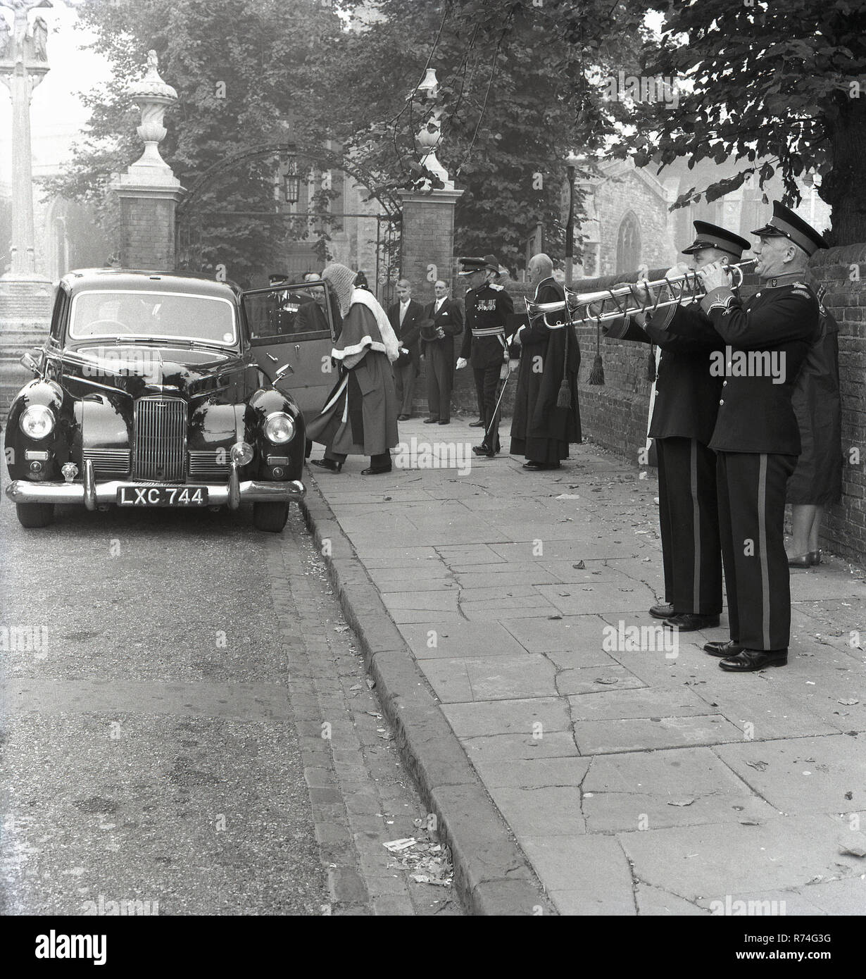 1967, históricos, dos varones de los trompetistas, posiblemente del Ejército de Salvación de pie sobre un pavimento tocando sus instrumentos como un coche oficial tira fuera de la Iglesia, como parte de un 'Best of British' desfile. Foto de stock