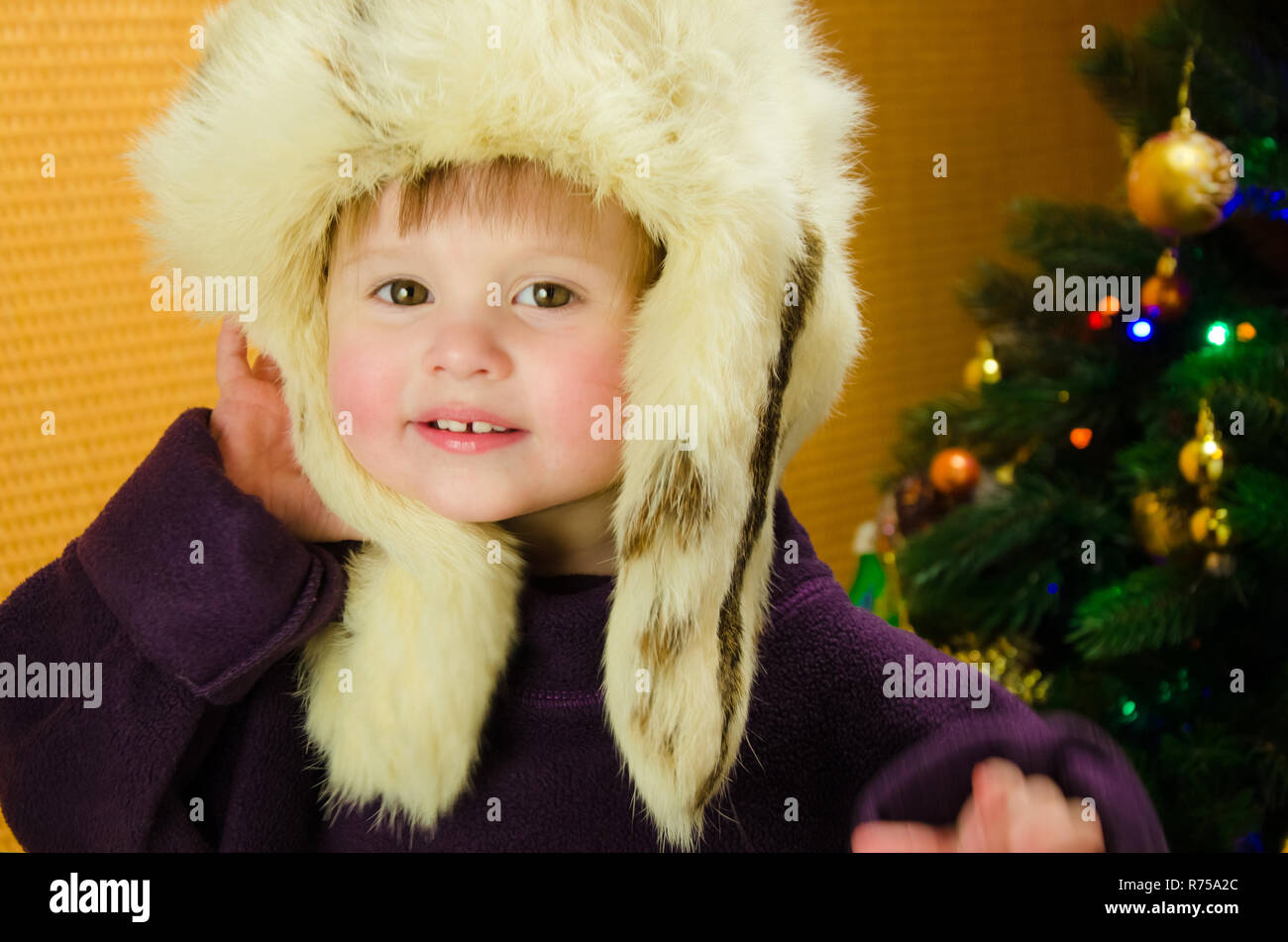 Retrato de dos años Pretty Little Girl en blanco, ruso, sombrero de piel cerca de un árbol de Navidad Foto de stock