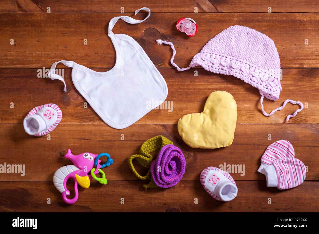 Juego de accesorios de ropa bebé, de algodón tejido rosado, juguetes y kid bib sobre fondo madera marrón, niño recién nacido tela moda niña, moderno Fotografía de stock -
