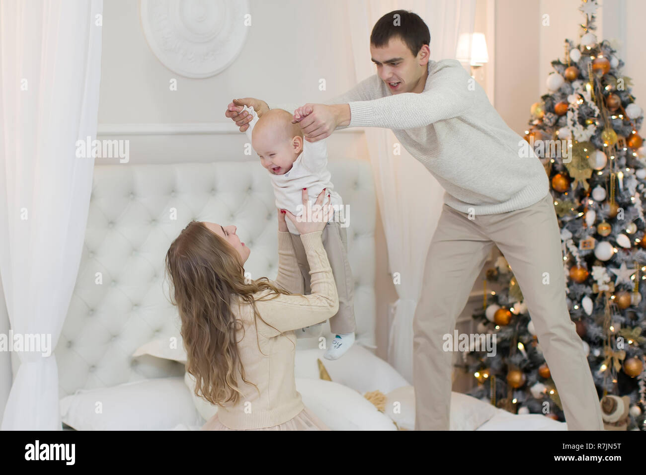 Papa Y Mama De Un Nino Pequeno En Una Gran Cama Blanca Jugando En El Fondo Del Arbol De Navidad Familia Joven Con Un Bebe En La Vispera De Ano Nuevo Fotografia