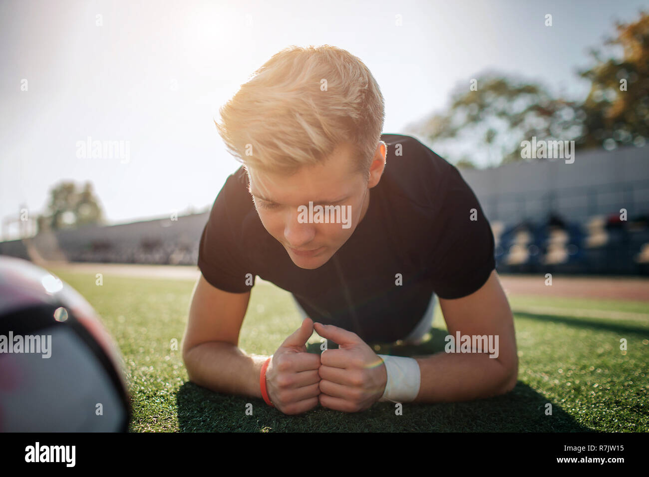 Joven rubia jugador de pie en posición de plancha sobre fútbol césped. Él está concentrada. Bola tumbado junto a él. Guy está solo. Foto de stock
