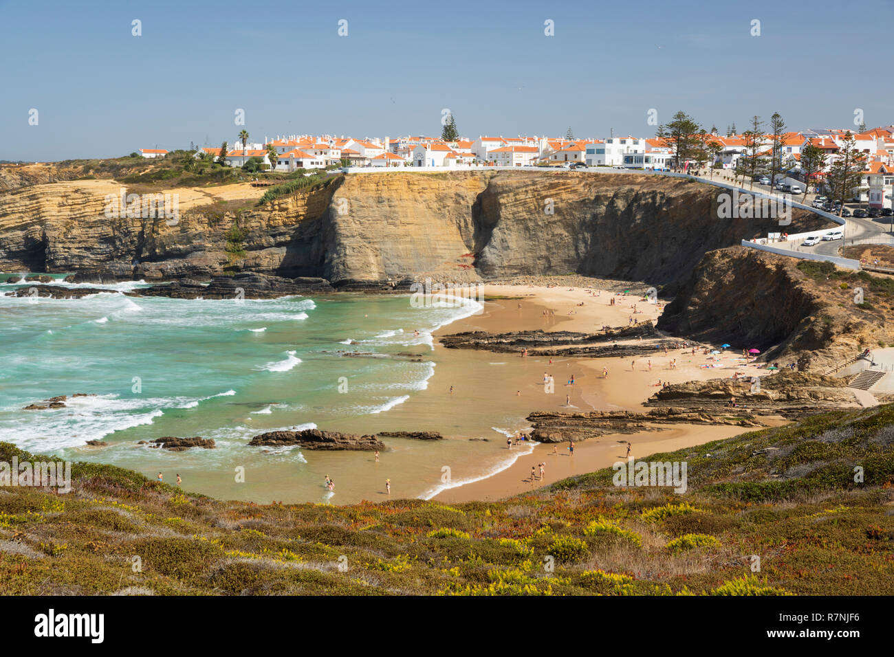 Ciudad encaladas en acantilados por encima de playa y olas del mar Atlántico en sol de mediodía, de Zambujeira do Mar, región de Alentejo, Portugal, Europa Foto de stock