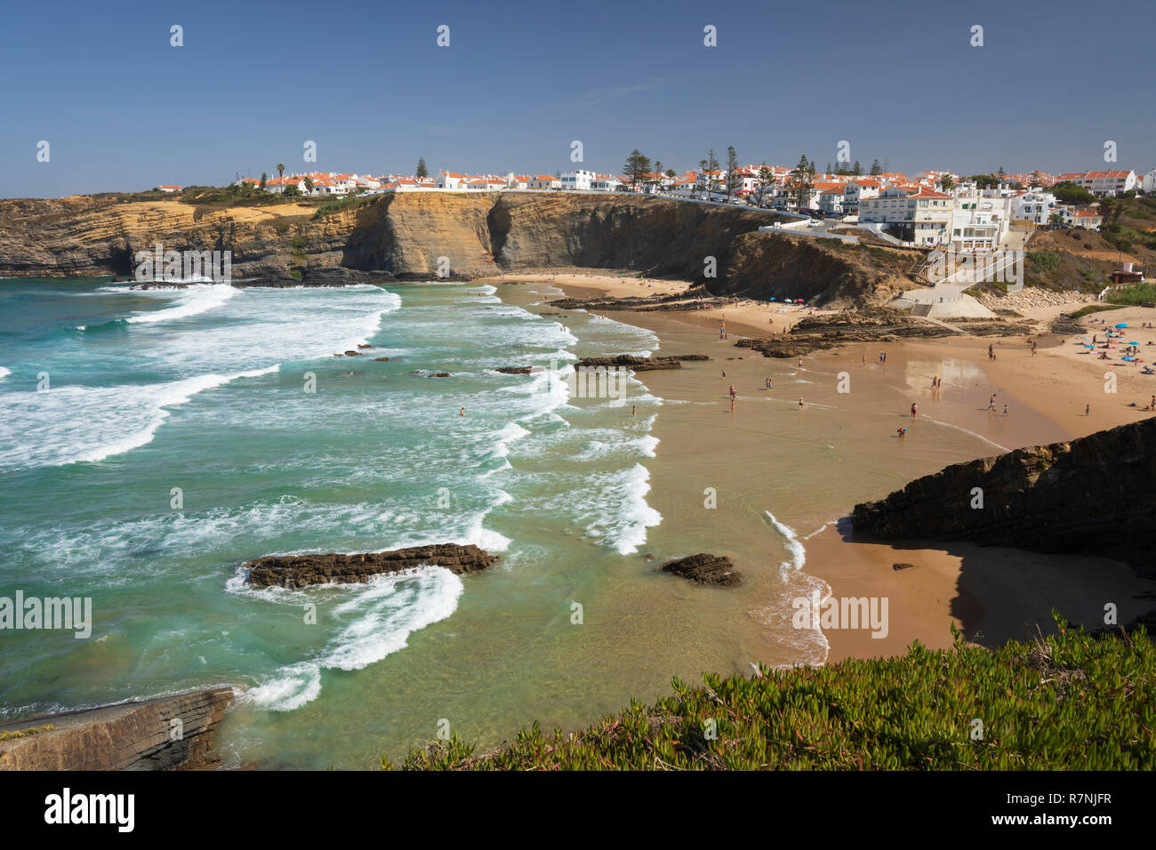 Ciudad encaladas en acantilados por encima de playa y olas del mar Atlántico en sol de mediodía, de Zambujeira do Mar, región de Alentejo, Portugal, Europa Foto de stock