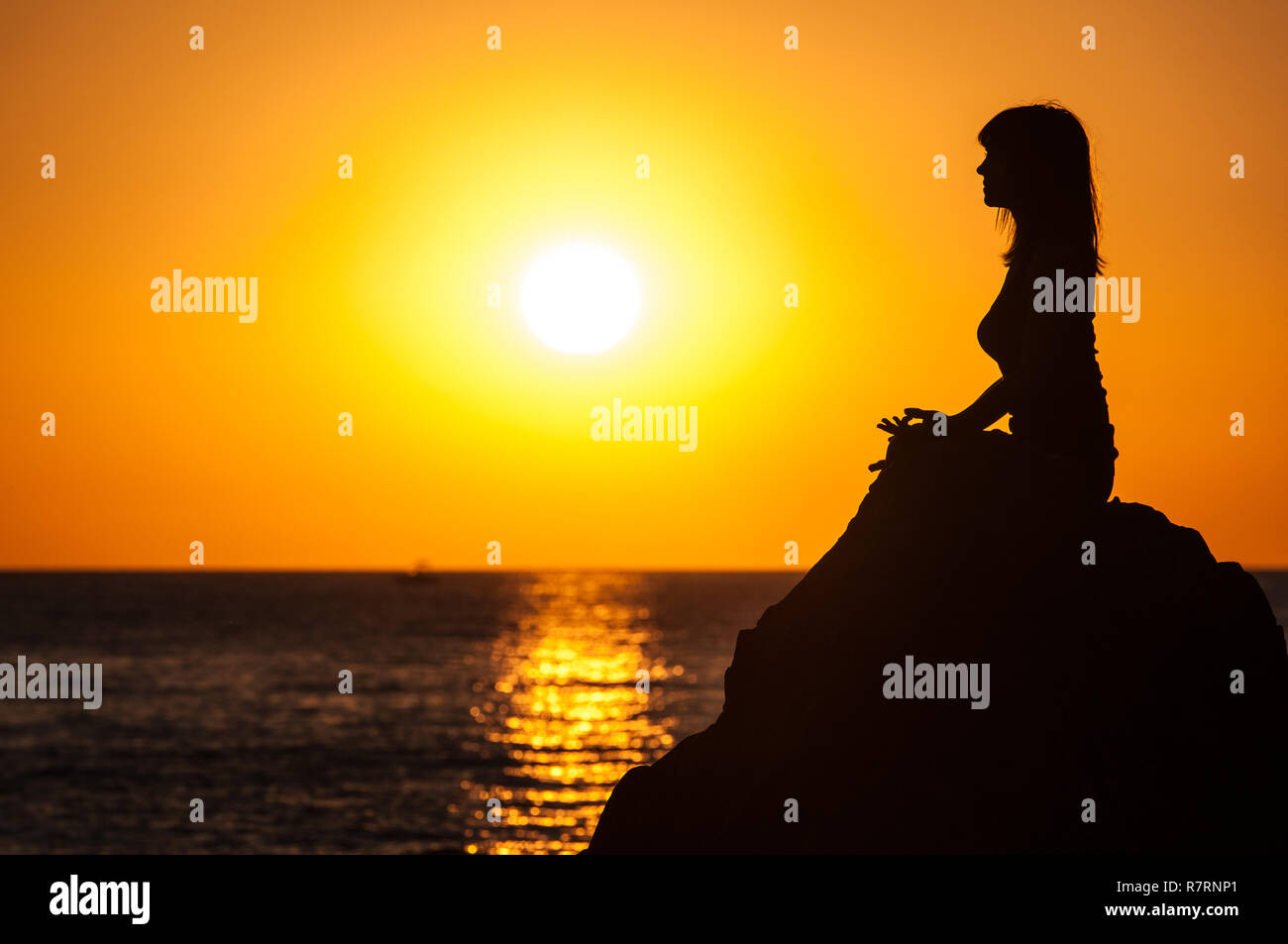 Argelès-sur-Mer (sureste de Francia). Alguien practicando yoga en las rocas, en frente de la playa al amanecer Racou. Hermosa joven con marrón Foto de stock