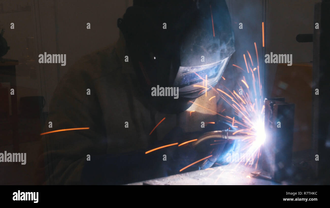 Un casco de soldador en hacer su trabajo. El proceso de soldadura. El humo y las chispas Foto de stock