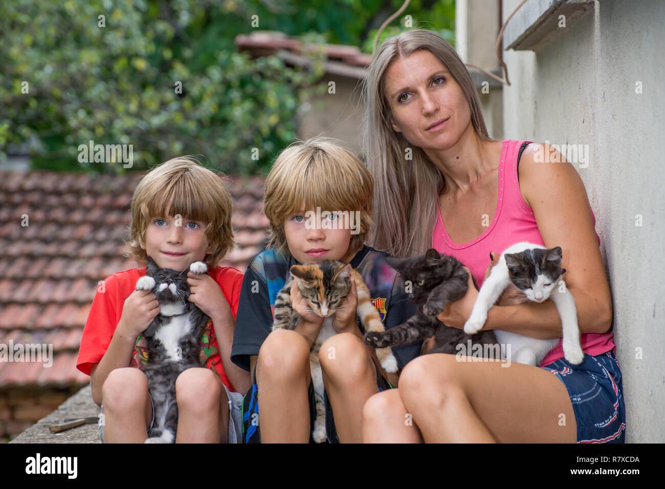 La madre con sus dos hijos, sentada y sosteniendo los gatos Foto de stock