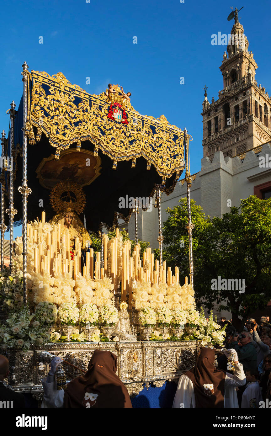 Los penitentes y lujosamente decorado flotar con la Santísima Virgen en la Semana Santa de Sevilla. En la parte superior derecha el morisco de la Giralda. La provincia de Sevilla, España, Andalusa Foto de stock