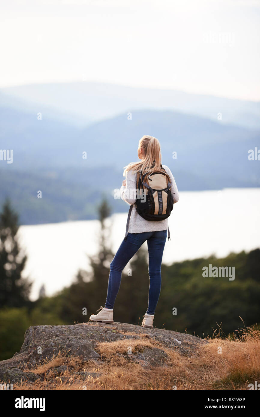 Un adulto joven mujer caucásica de pie solo en la roca después de largas caminatas, admirando la vista del lago vista posterior Foto de stock