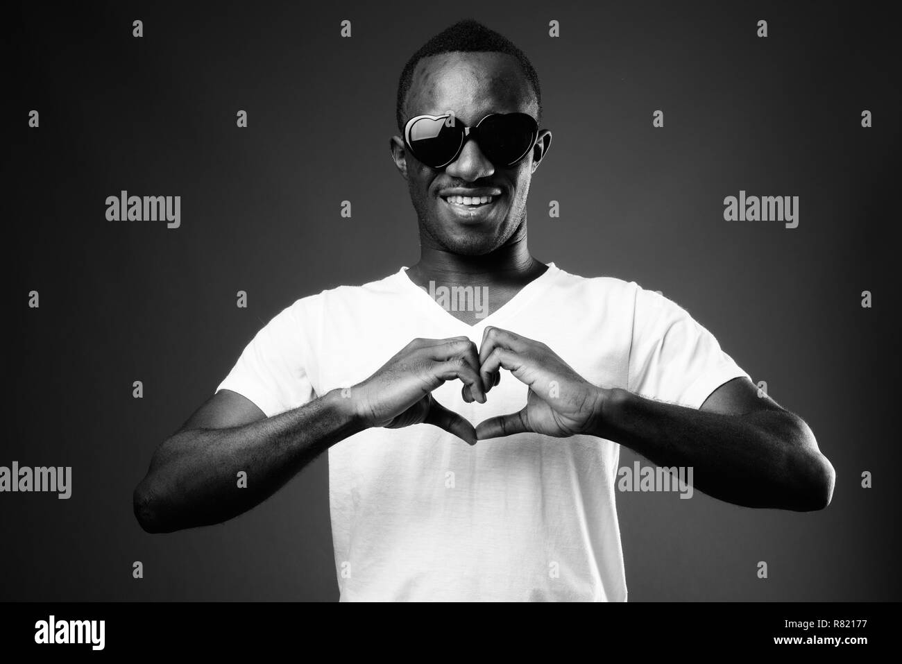 El hombre africano joven con gafas de sol mientras se hace signo del corazón Foto de stock