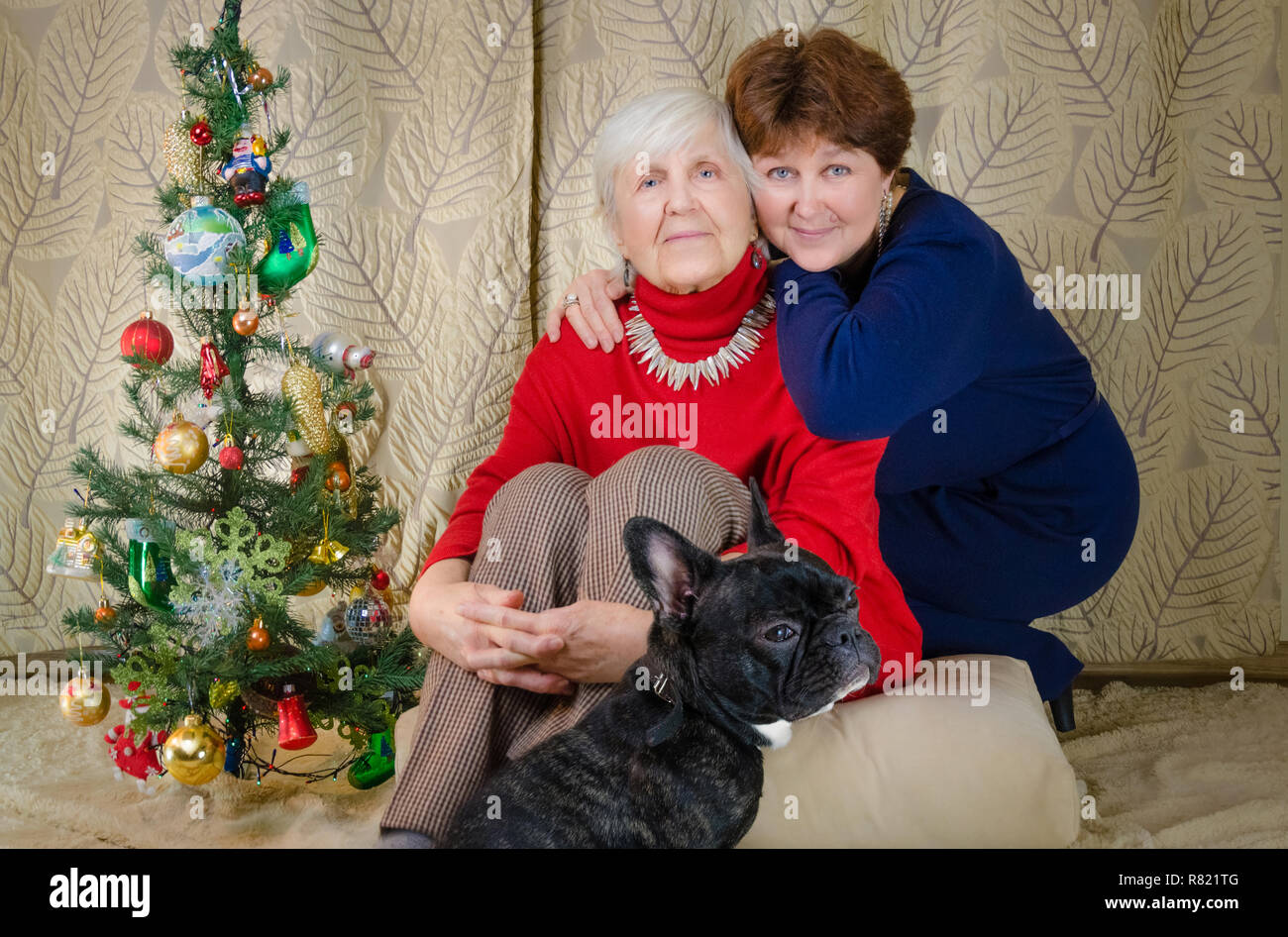 Momentos familiares en el tiempo de Navidad. mujer vieja sonrisa. abuela y su hija están sentados cerca del árbol de Navidad. espíritu de Año Nuevo abrazo entre sí. Foto de stock