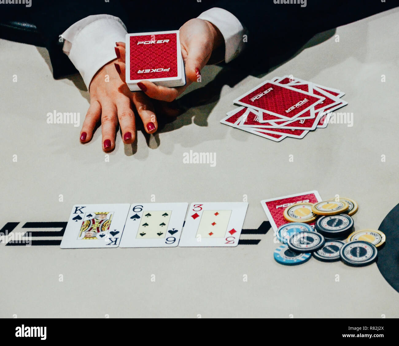 Cerca de mujeres repartidor con una baraja de cartas en la mano después del tratamiento 3 cartas sobre la mesa, con fichas de póquer en el lado - Torneo de Texas hold 'em Foto de stock