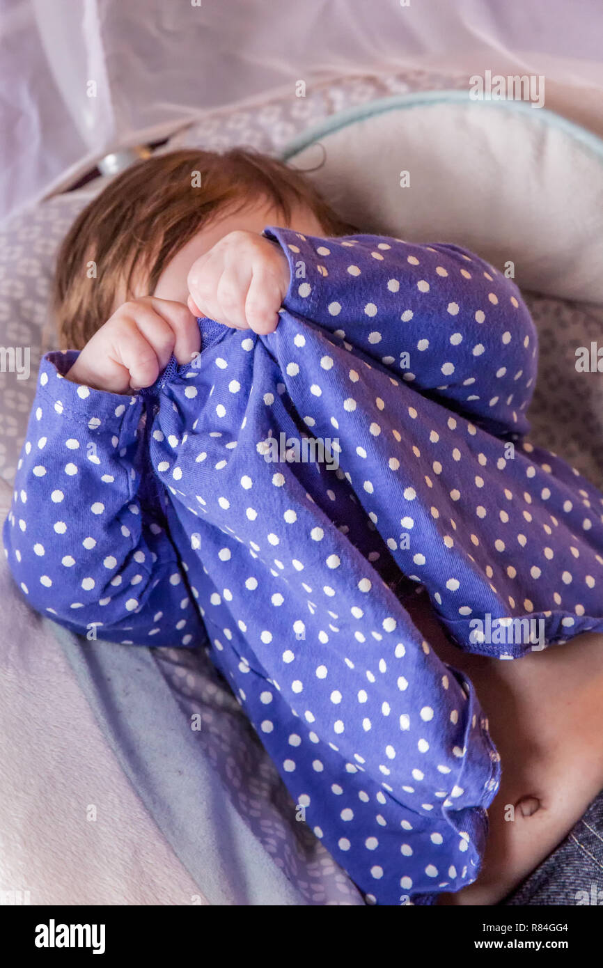 Lily hace tres meses jugando peek-a-boo con su vestido para cubrir sus ojos. (MR) Foto de stock