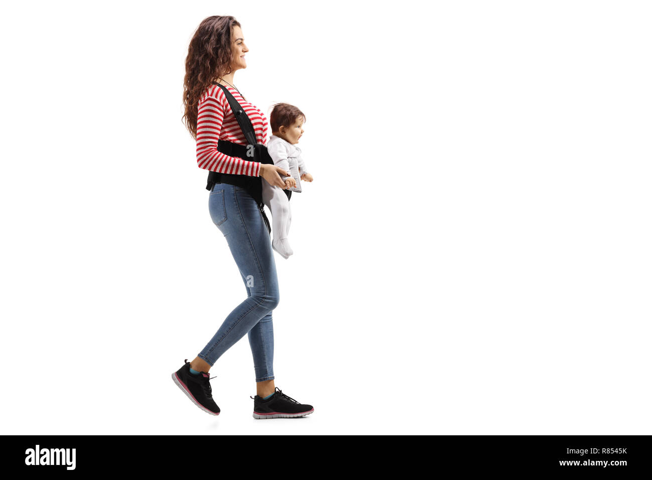 Disparo de longitud completa de una madre joven con un bebé en un portador caminar aislado sobre fondo blanco. Foto de stock