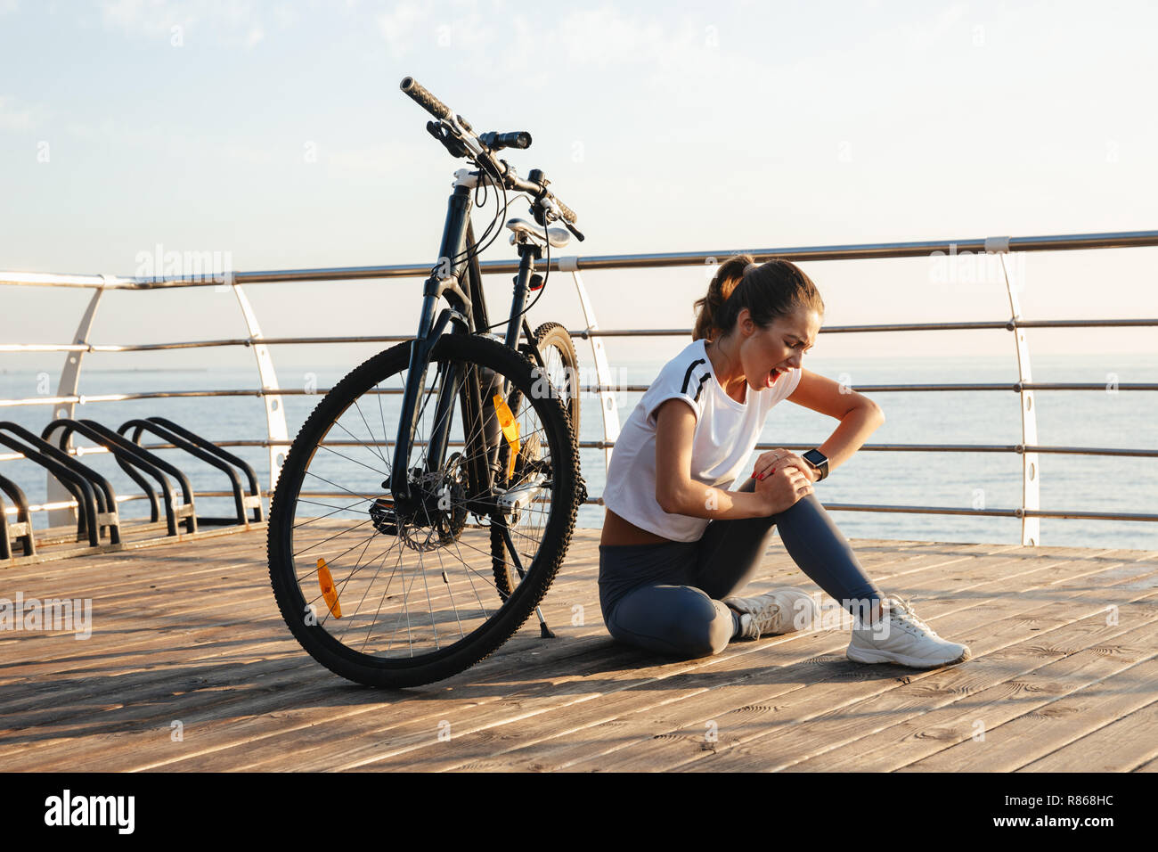 Joven y bella chica de gimnasia al aire libre con una bicicleta, sentarse,  sufriendo un dolor de rodilla Fotografía de stock - Alamy