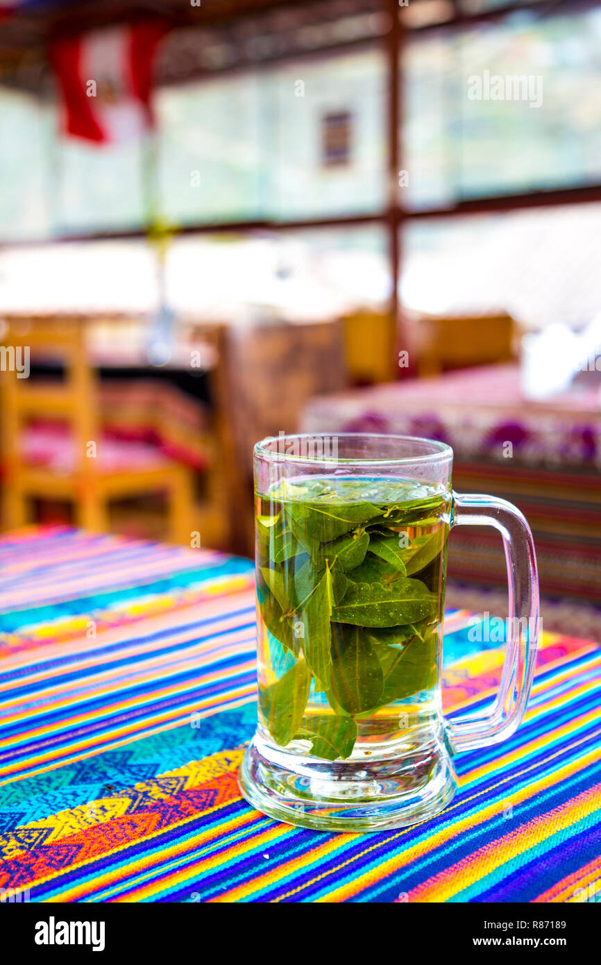 Un vaso de té de coca peruana sobre una mesa con coloridos manteles tradicionales, Perú Foto de stock