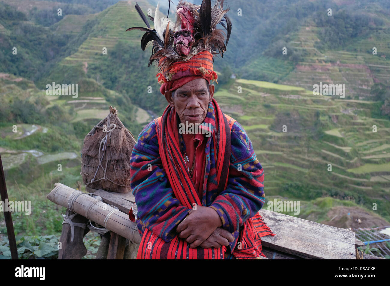 Un anciano Ifugao hombre llevando sombreros adornados con plumas y monkey cráneo en las terrazas de arroz de Banaue.... en el norte de Luzón, Filipinas. En el pasado los Ifugao, también conocido como el Ifugaw, Yfugao Ipugao, eran de temer head-hunters, así como otras tribus en las regiones montañosas del norte de Luzón. Foto de stock