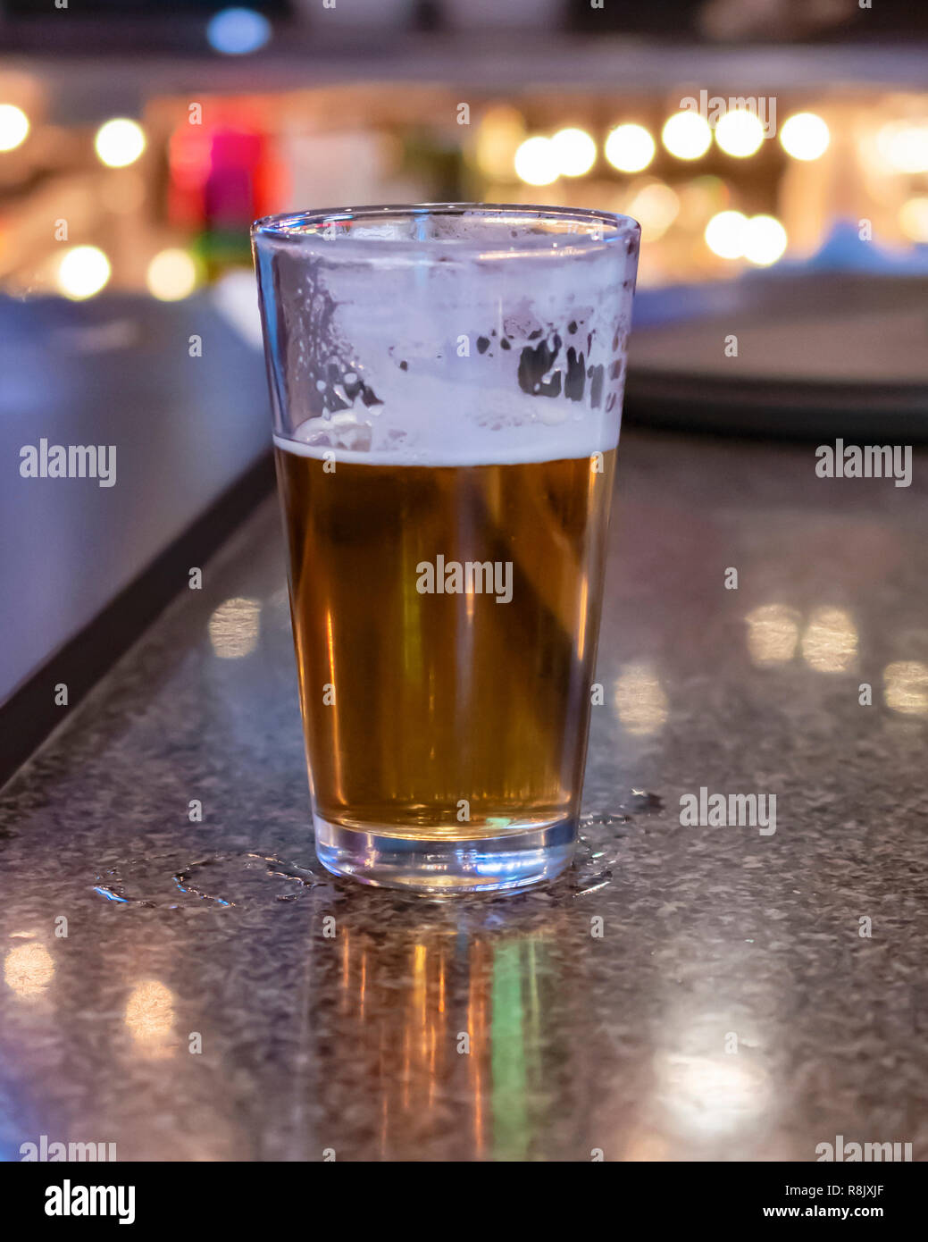 Un borracho medio vaso de cerveza en el bar. Fondo difuminado. Luces Bokkeh. Foto de stock