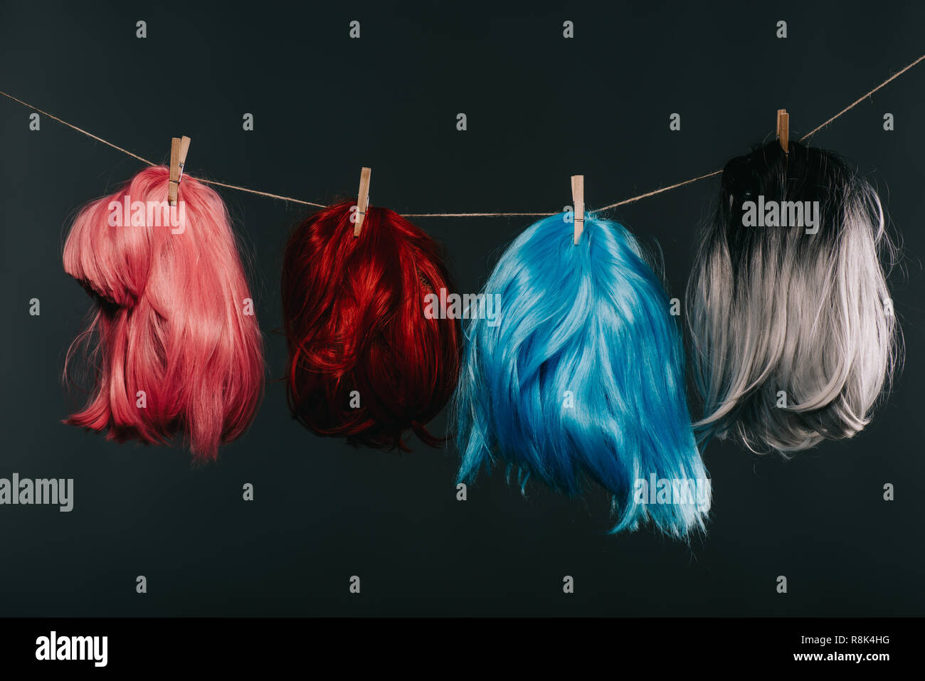 Cuatro coloridos pelucas colgando de cuerdas aisladas sobre negro Foto de stock
