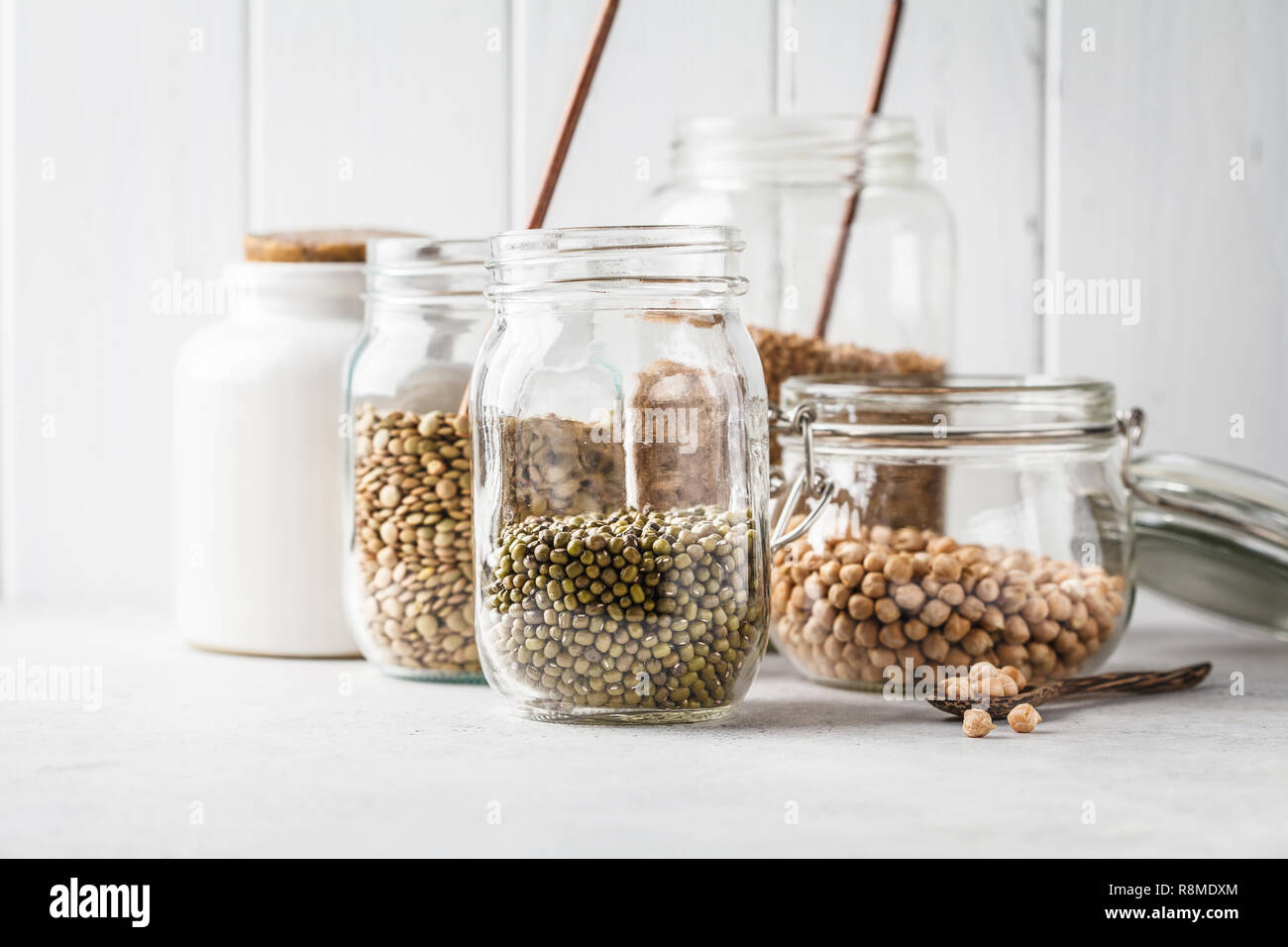 Diversas leguminosas: frijoles, garbanzos, lentejas, trigo sarraceno en tarros de vidrio sobre un fondo blanco. Saludable comida vegetariana, proteína vegetal, a base de vegetales morir Foto de stock