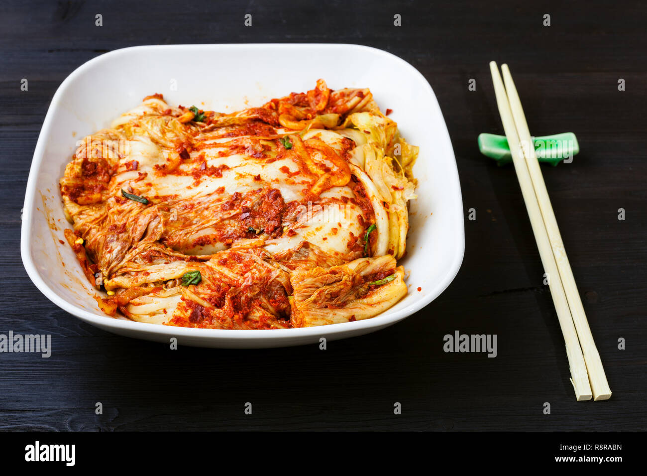 - Cocina coreana Kimchi picante aperitivo (repollo) nappa en blanco tazón y palillos de mesa de madera de color marrón oscuro Foto de stock