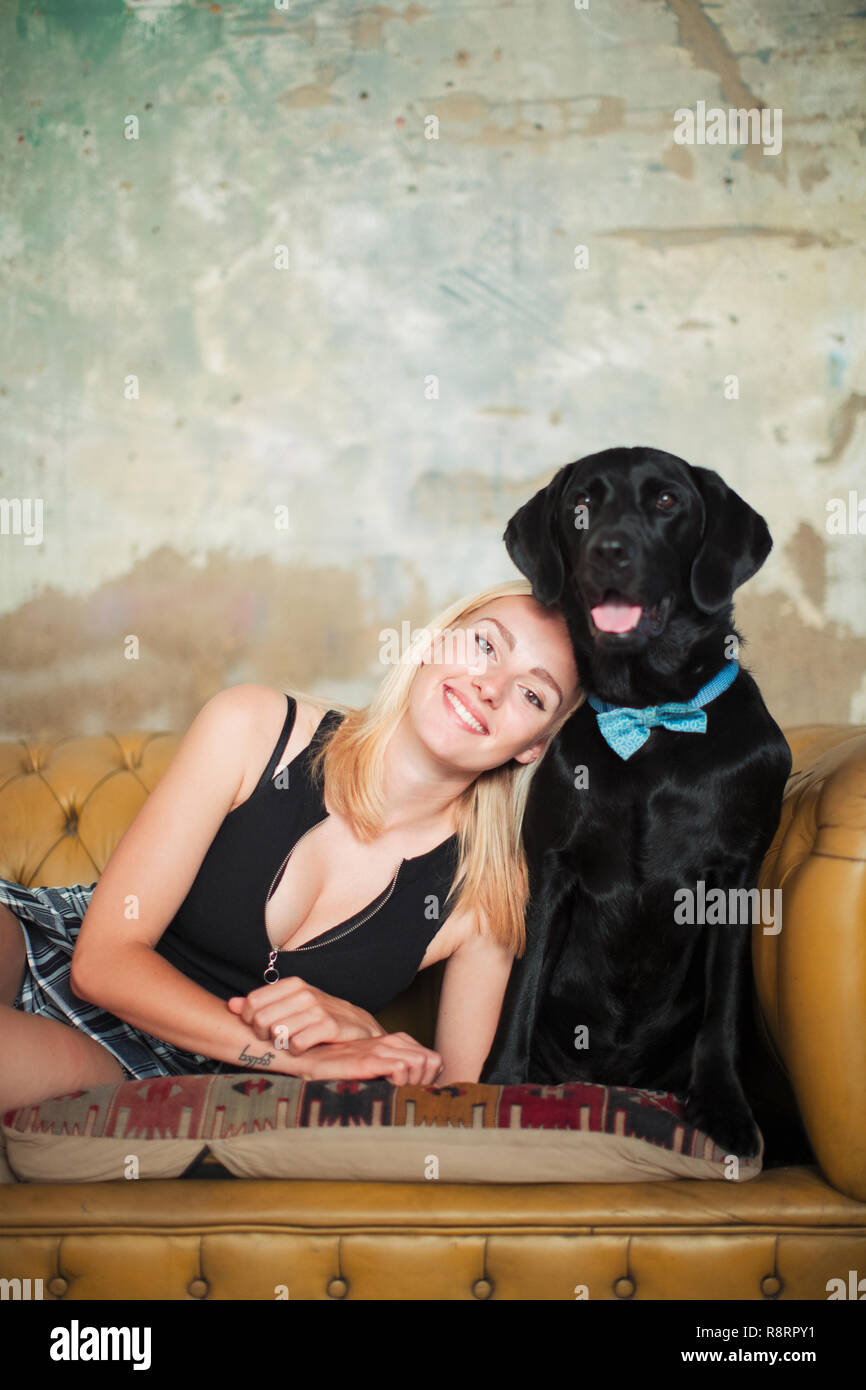 Retrato sonriente, despreocupado joven con perro negro vestidos de pajarita en el sofá Foto de stock