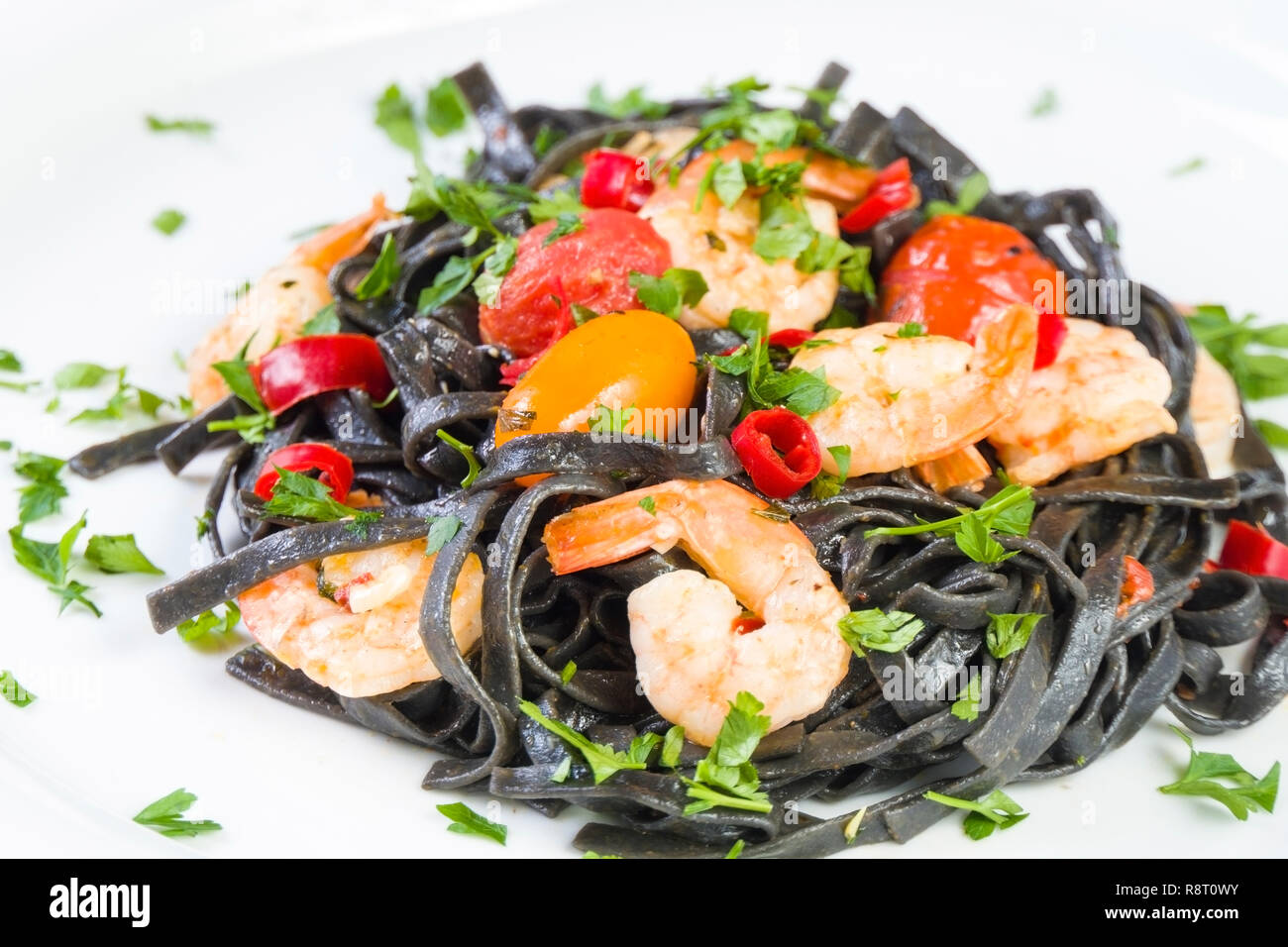 Tinta de calamar negro Fettuccine Pasta con langostinos o gambas tomates cherry, el perejil, la guindilla en el vino y la salsa de mantequilla. Foto de stock