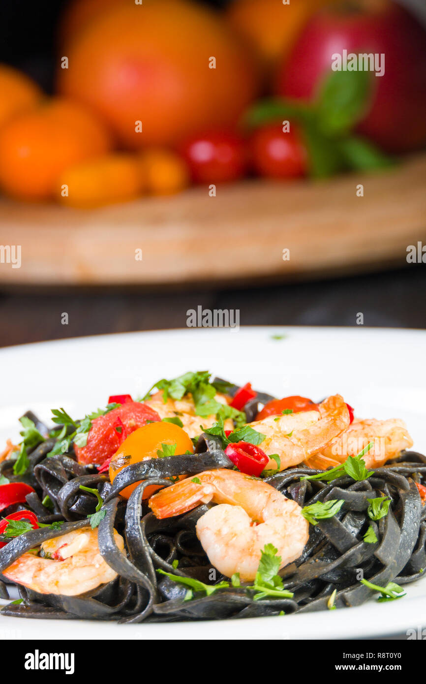 Tinta de calamar negro Fettuccine Pasta con langostinos o gambas tomates cherry, el perejil, la guindilla en el vino y la salsa de mantequilla. Foto de stock