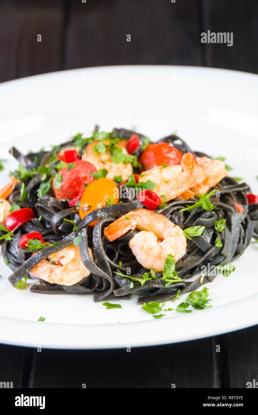 Tinta de calamar negro Fettuccine Pasta con langostinos o gambas tomates cherry, el perejil, la guindilla en el vino y la salsa de mantequilla. Foto de stock