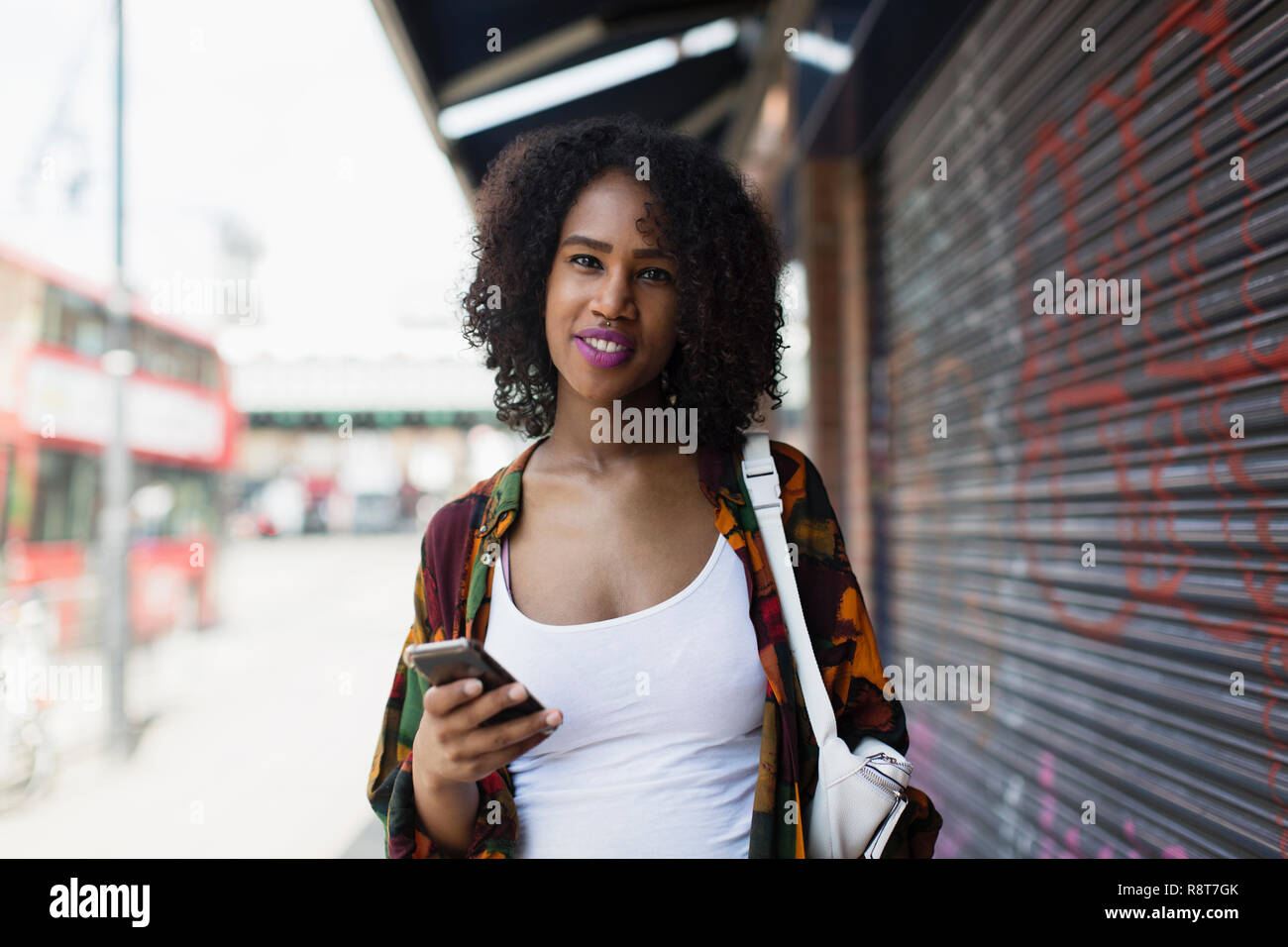 Retrato sonriente, confía en mujer joven con smart phone en la acera urbana Foto de stock