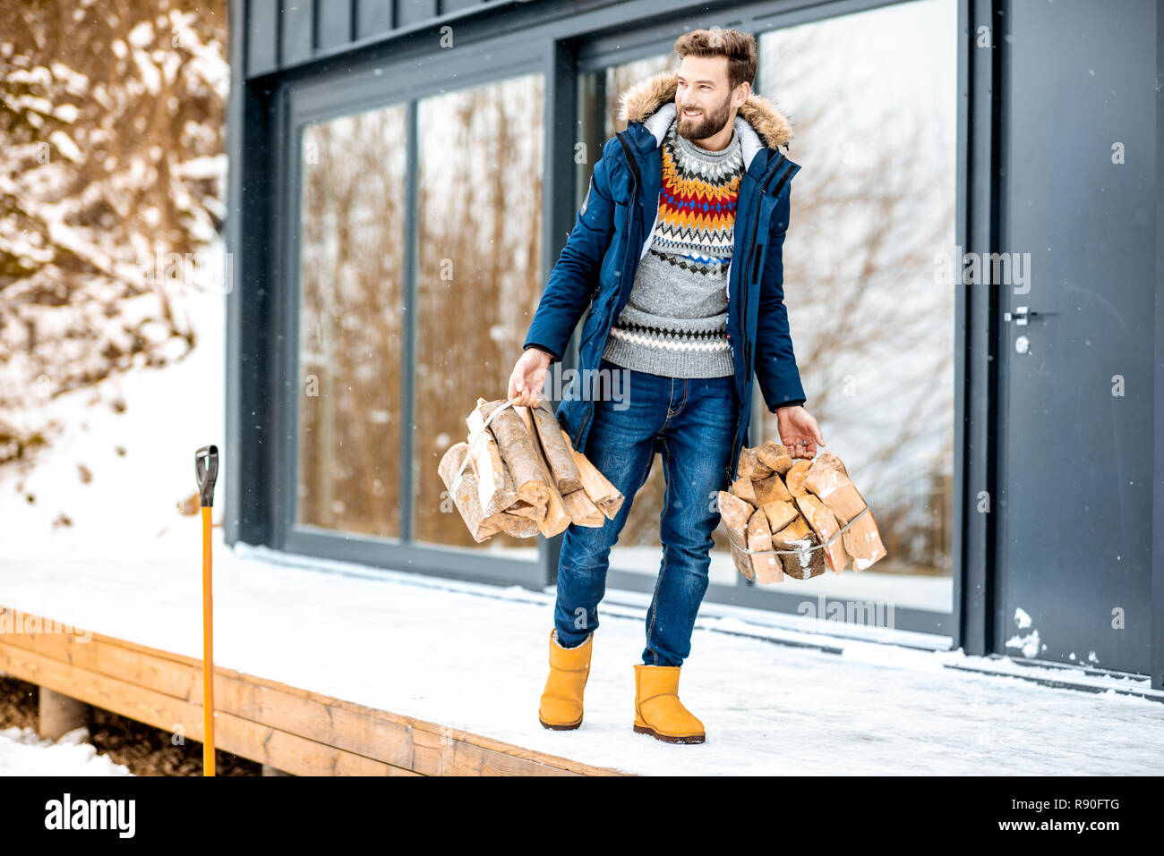 Guapo en ropa de invierno leñas en la terraza cerca de la casa en las Fotografía de stock - Alamy