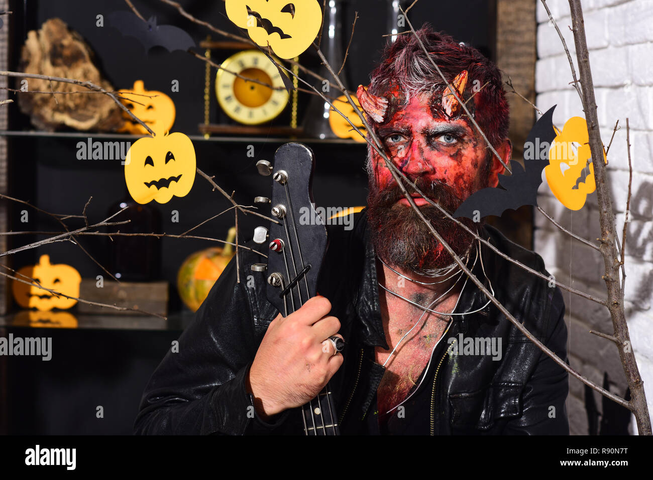 Concepto de fiesta de Halloween. Hombre vestido con miedo detrás de Maquillaje de Halloween calabazas y murciélagos decoración. Demonio con cuernos y cara de miedo tiene black guitarra eléctrica. Diablo o monster Concepto de fiesta de Halloween. Hombre vestido con miedo detrás de Maquillaje de Halloween calabazas y murciélagos decoración. Demonio con cuernos y cara de miedo tiene black guitarra eléctrica. Diablo o monster