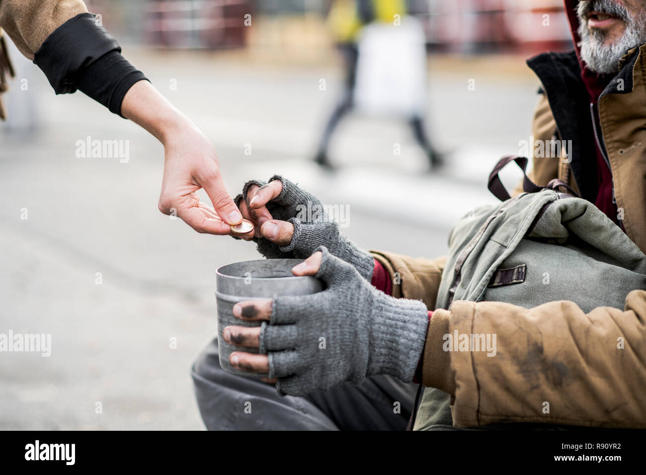 Una vista de sección media de la mujer dando dinero al mendigo sin hogar hombre sentado en la ciudad. Foto de stock